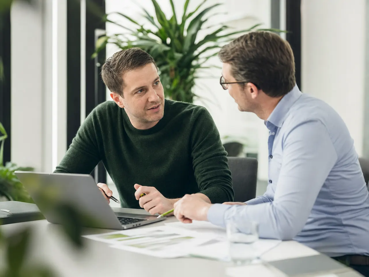 IT-Berater und Kunde besprechen Unterlagen und Laptop am Besprechungstisch