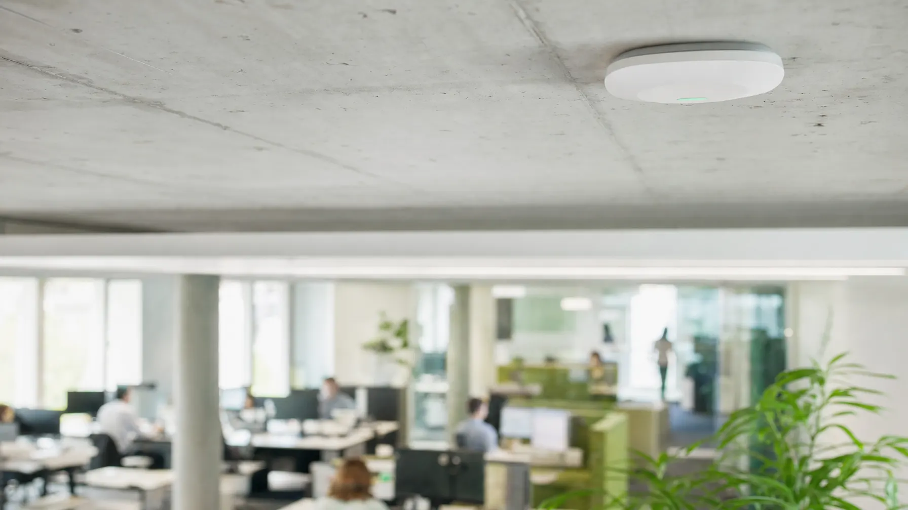 Access Point an der Decke eines hellen Großraumbüros mit arbeitenden Menschen im Hintergrund