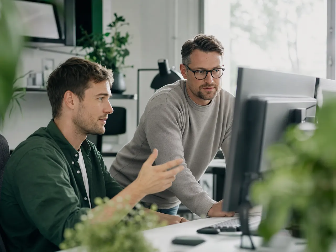 Zwei IT-Fachkräfte besprechen sich vor Monitoren in einem hellen Büro