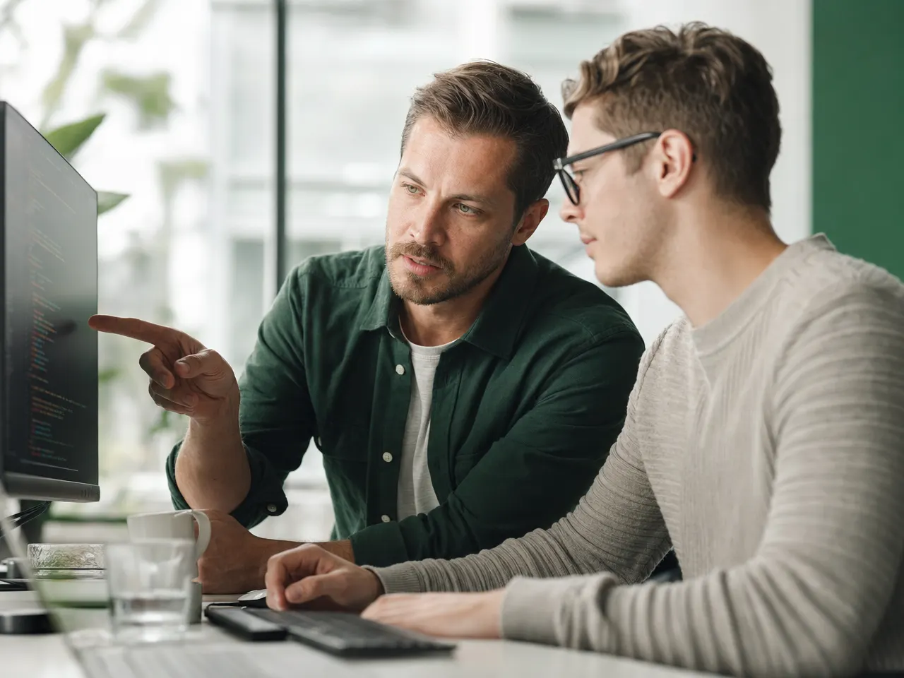 Zwei Entwickler besprechen einen Programmablauf vor einem großen Bildschirm