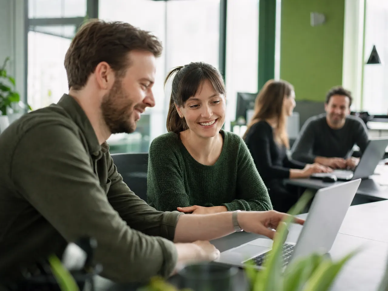 IT-Fachleute in lockerer Arbeitssituation an Laptops im Büro